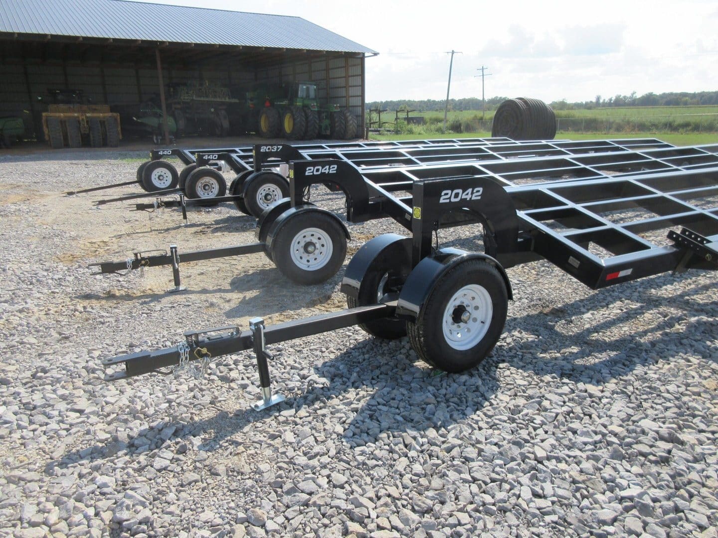 Black flatbed trailers in a gravel lot.