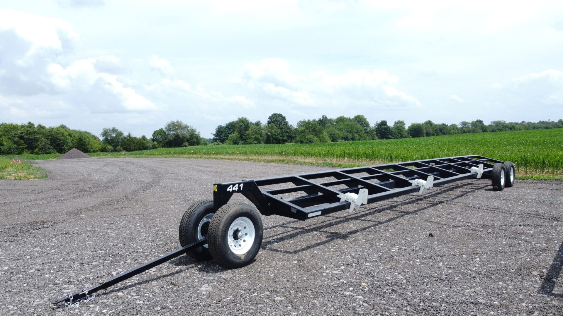 Black flatbed trailer with wheels on gravel.