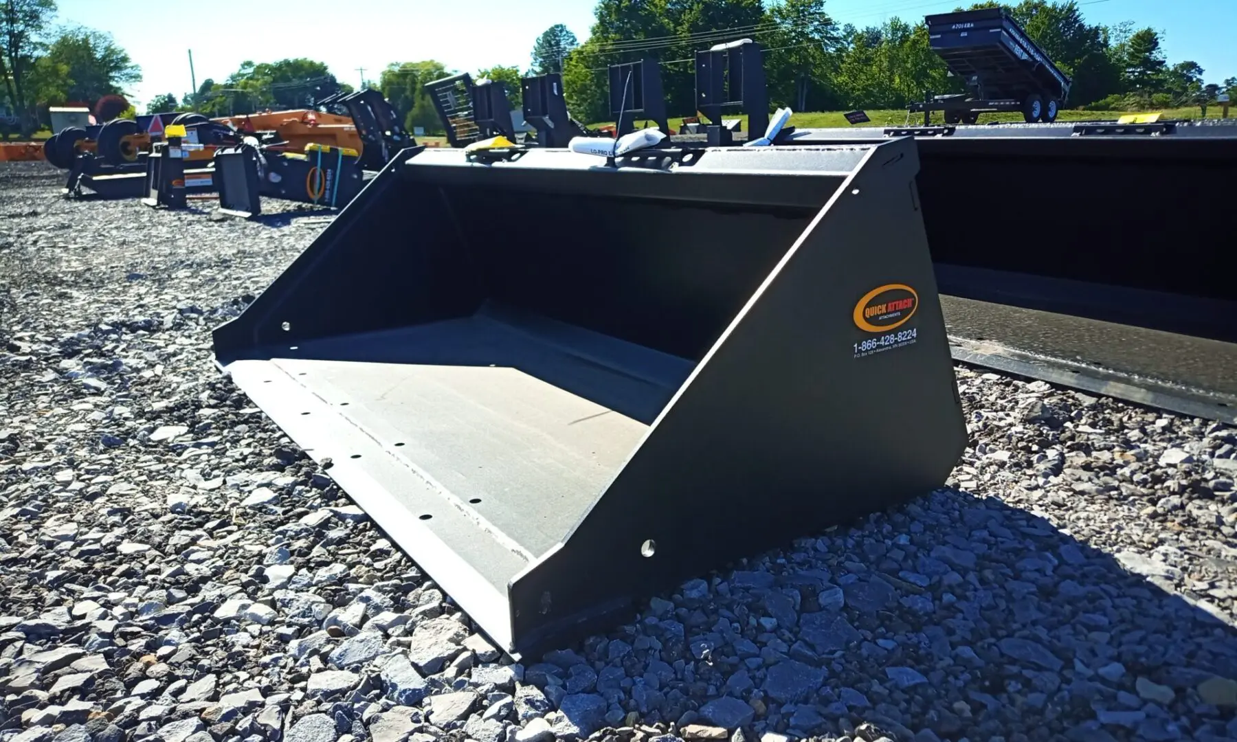 Black tractor bucket on gravel ground.