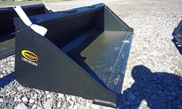 Black metal tractor bucket on gravel.