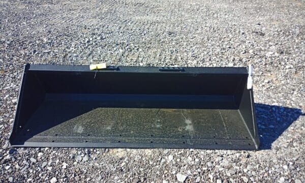 Black tractor bucket on gravel ground.