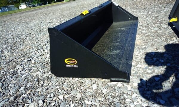 Black tractor bucket on gravel ground.