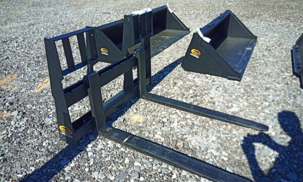 Black forklift attachments on gravel.