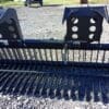 Black metal grapple rake on gravel.