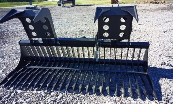 Black metal grapple rake on gravel.