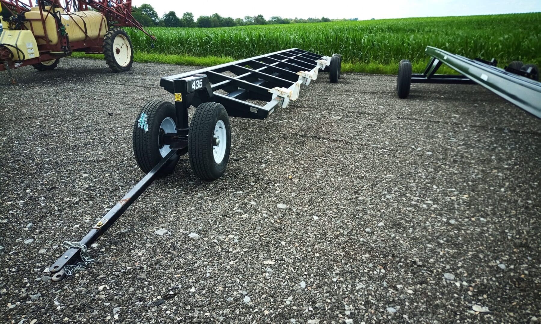 Black farm trailer with wheels on gravel.