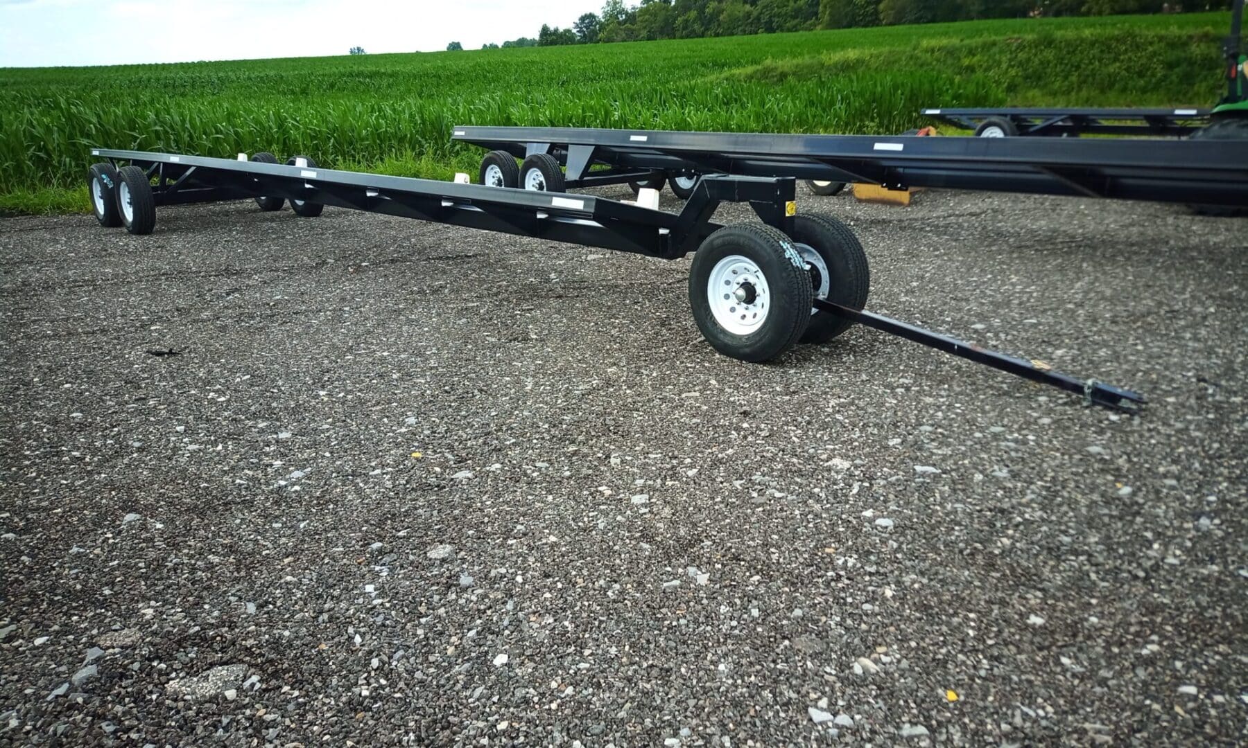 Black utility trailer with wheels on gravel.