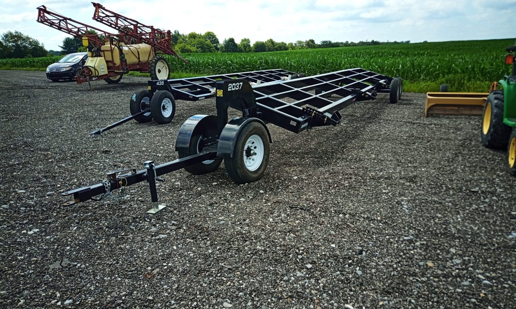 Black flatbed trailer with wheels on gravel.