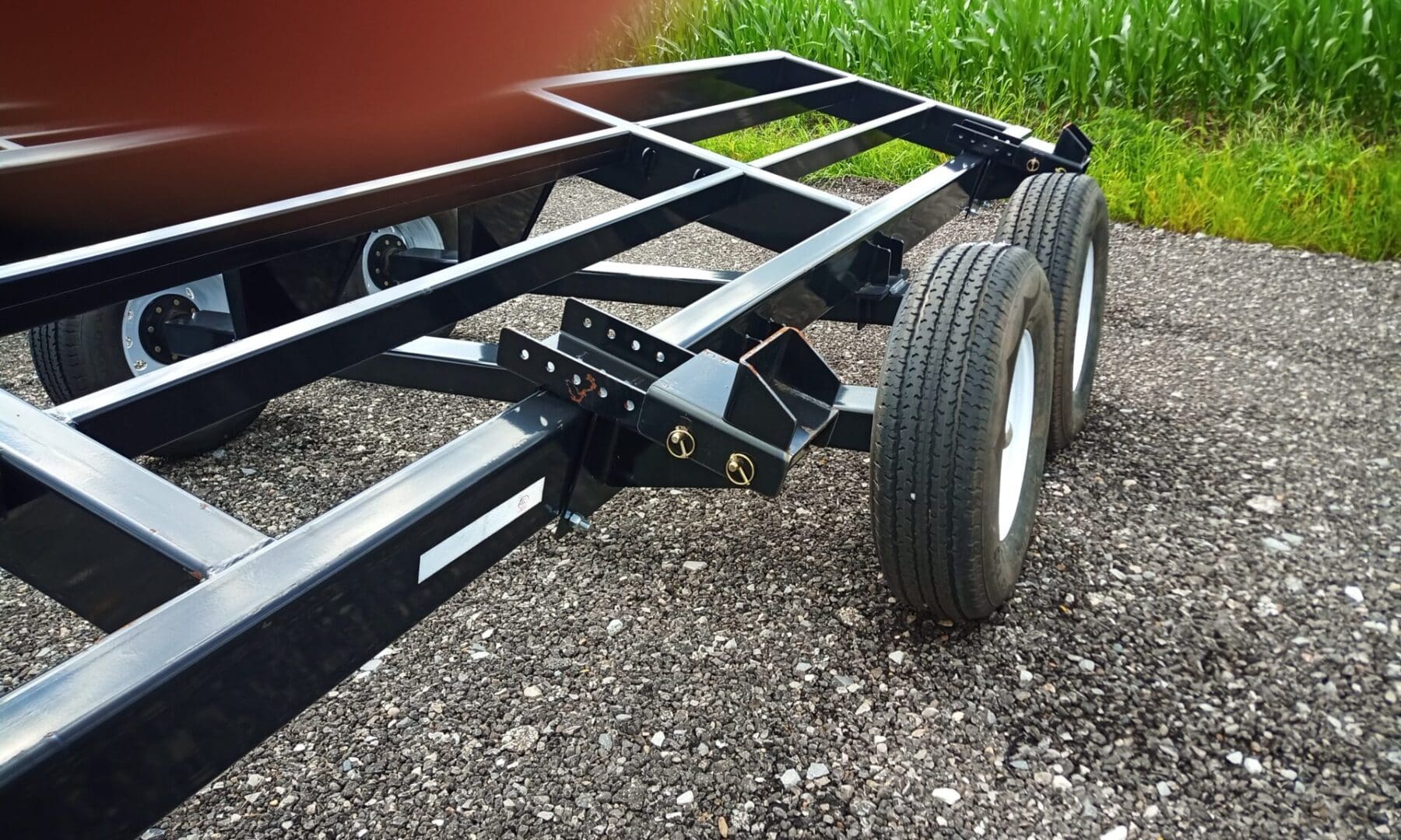 Black trailer with three tires on gravel.