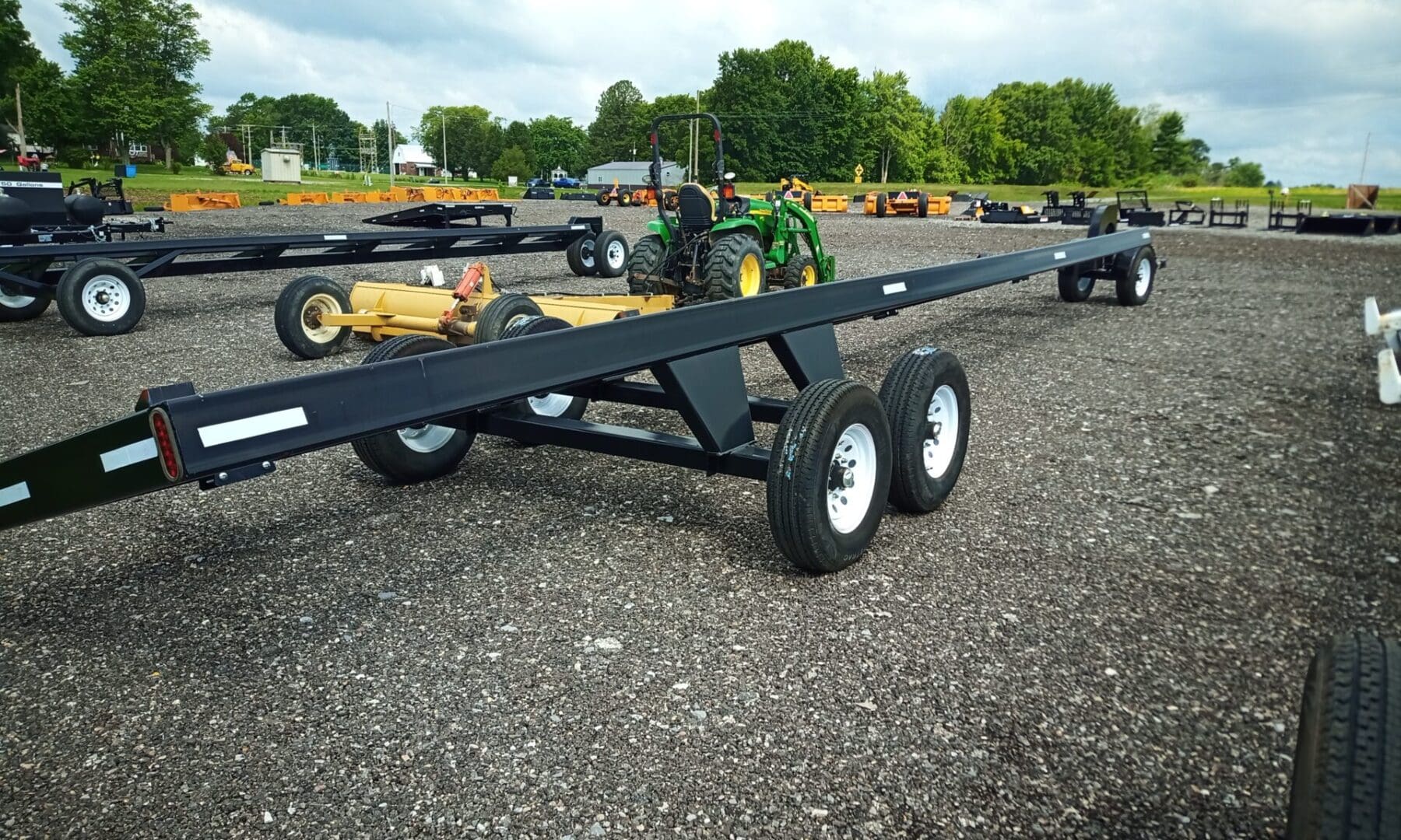 Black trailer with four wheels on gravel.