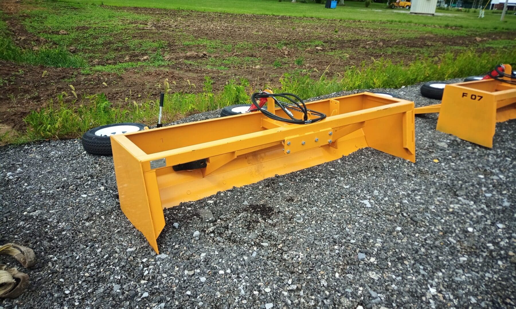 Yellow grader blade on gravel surface.