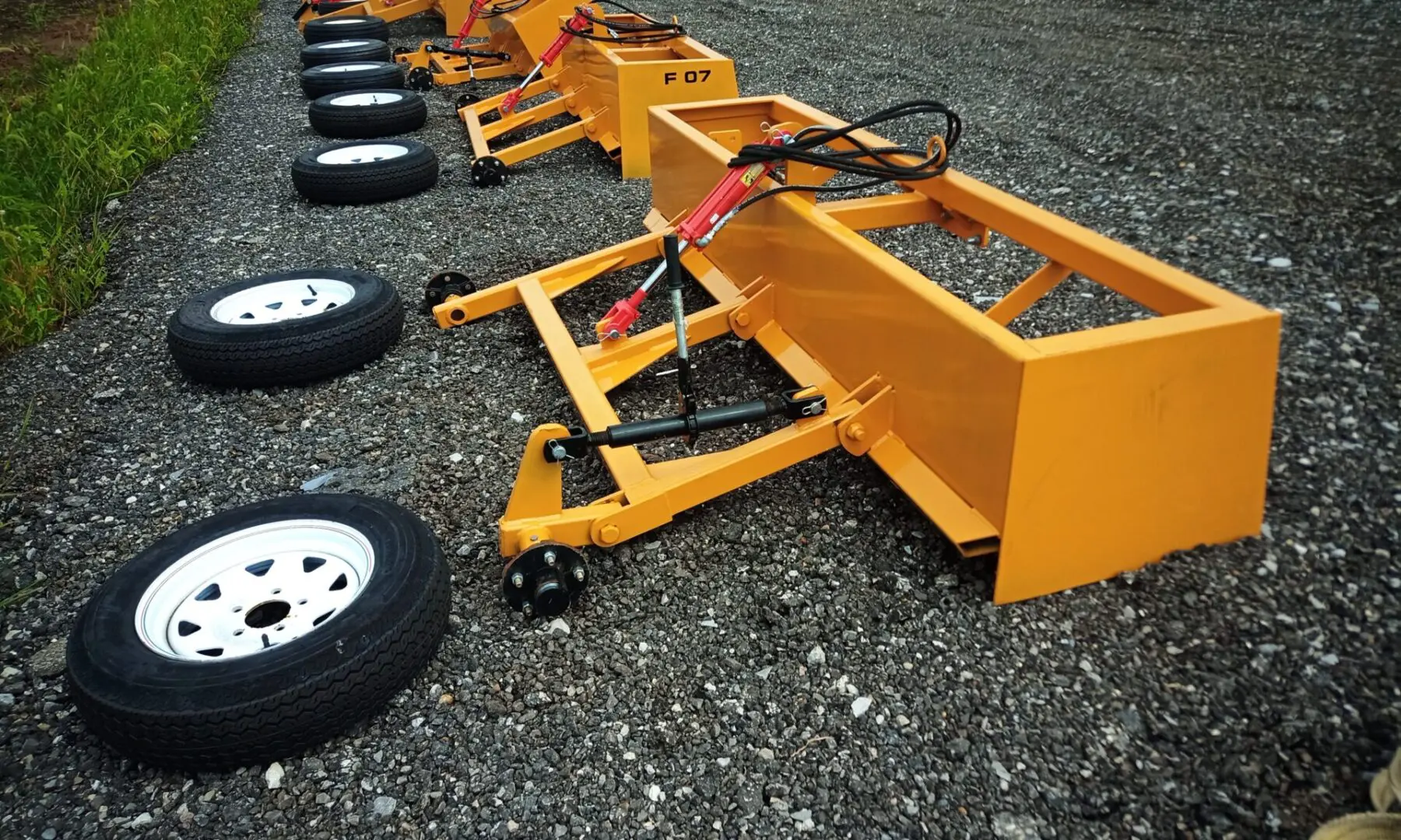 Yellow box blade with wheels on gravel.