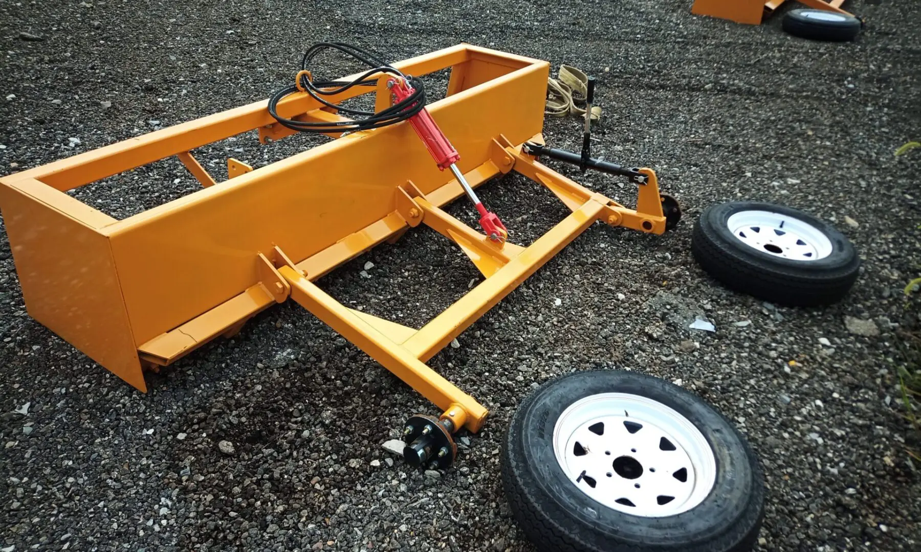 Yellow farm equipment with wheels on gravel.