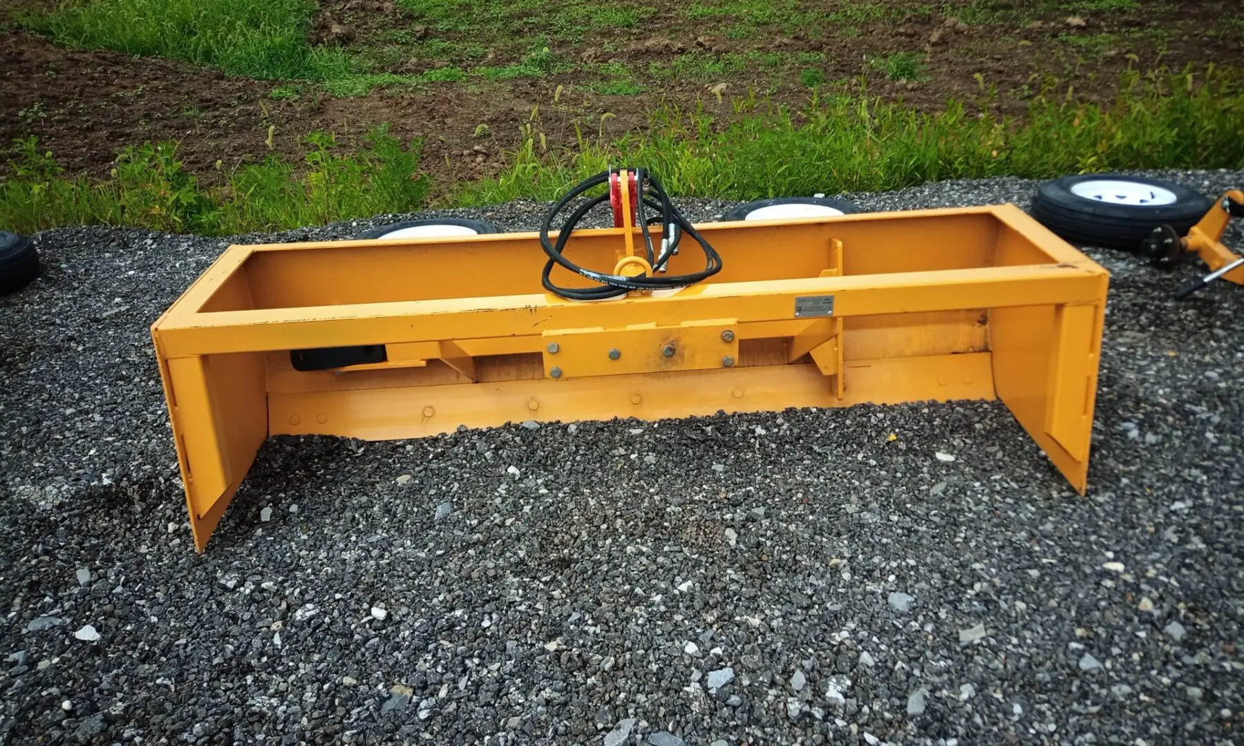 Yellow tractor snow plow attachment on gravel.