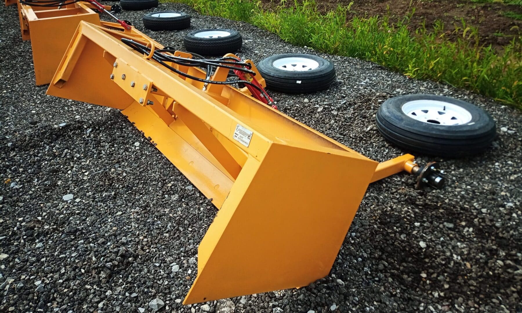 Yellow grader blade on gravel ground.