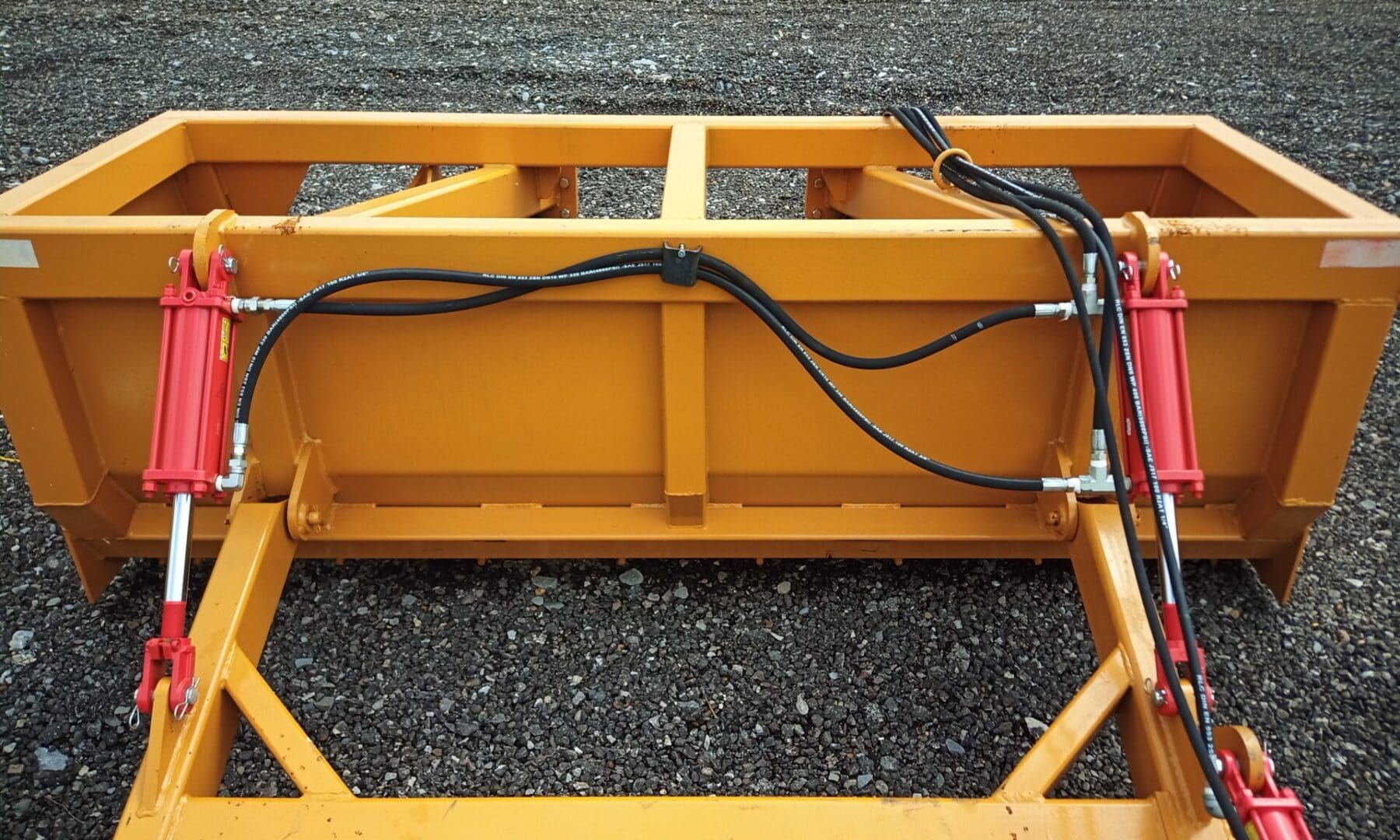 Yellow tractor attachment with hydraulic hoses.