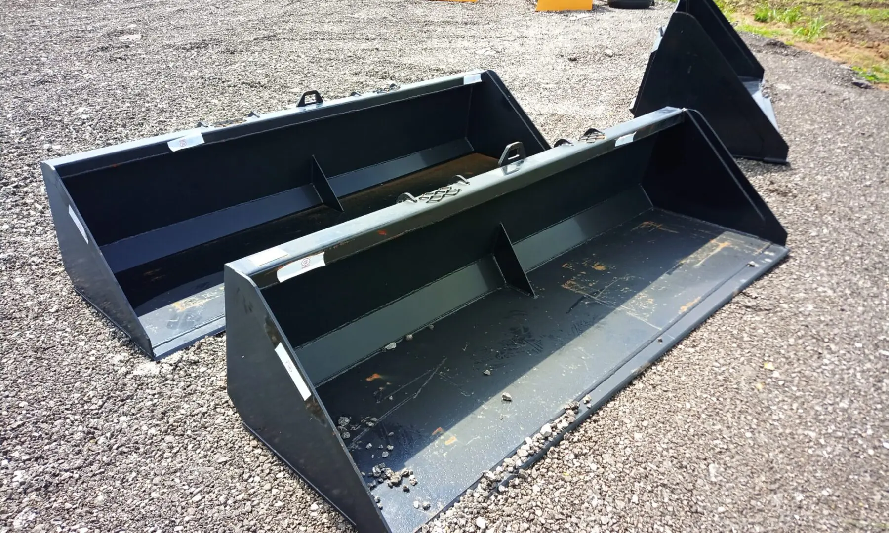 Two black tractor buckets on gravel.