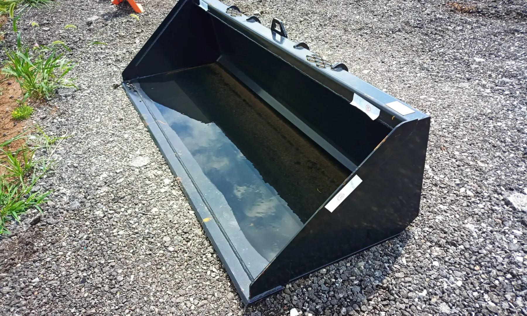 Black metal tractor bucket on gravel.