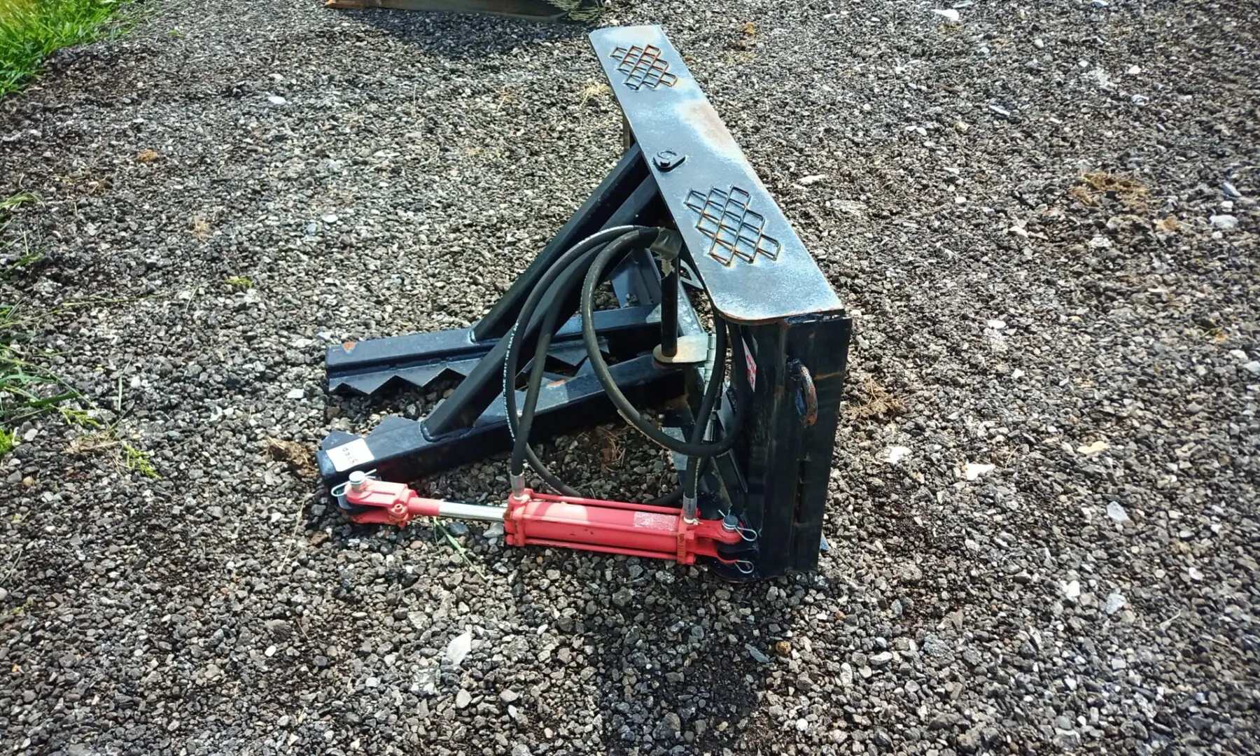 Black hydraulic tree grapple on gravel.