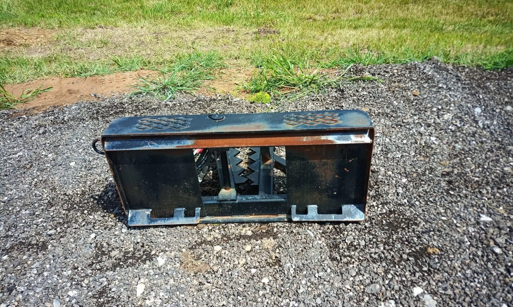 Black metal tractor attachment on gravel.