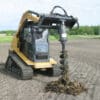 Tracked skid steer with auger digging hole.
