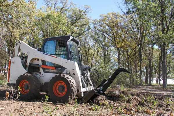 White skid steer clearing land.