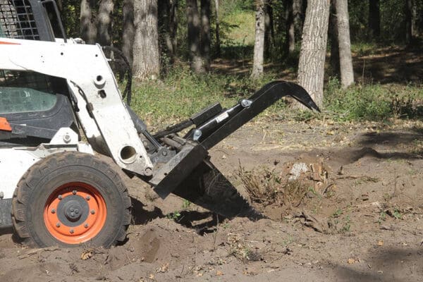 Bobcat removing tree stump with grapple.