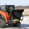Orange tracked skid steer spreading salt.