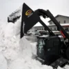 Here's an alt tag for the image: Skid steer removing snow with bucket.