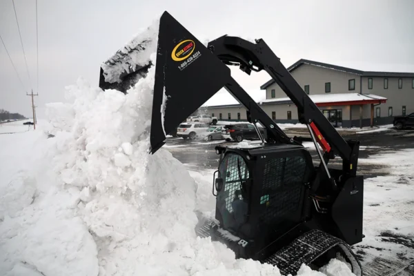 Here's an alt tag for the image: Skid steer removing snow with bucket.