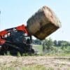 Tracked skid steer lifting hay bale.