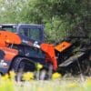 Orange skid steer cutting bushes.