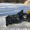 Snow plow attached to yellow excavator.