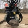 Skid steer grapple lifting rock.