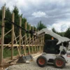 Skid steer installing fence posts.